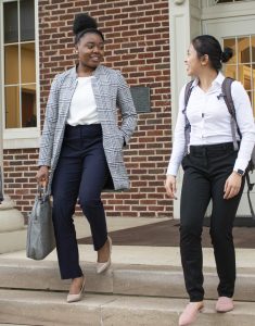 Two female university students walk down steps outside a brick building