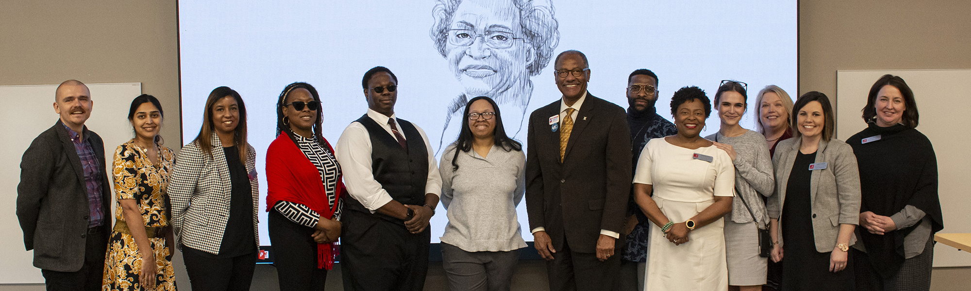 a group of people standing in front of a projection screen with an image of Ethel Hall