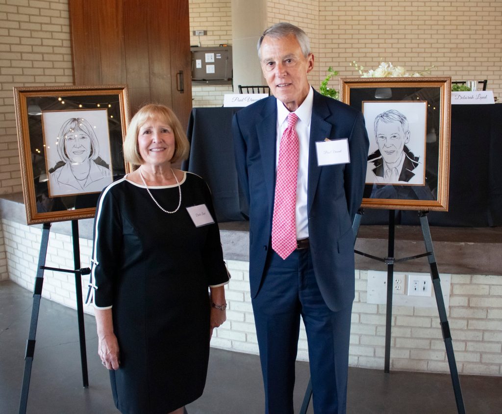 A man and woman pose next to hand-drawn photos of them during a ceremony