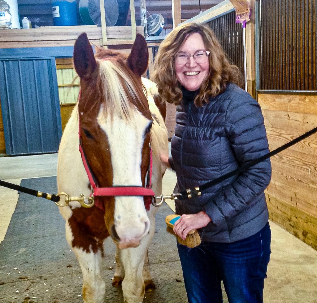 A female university researcher poses for a photo next to a horse