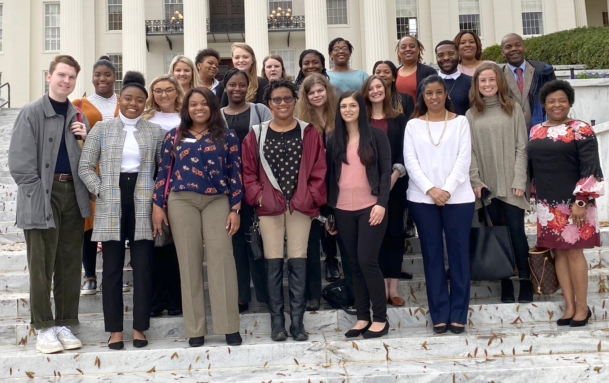 Male and female university students pose for a photo outside of a legislative building