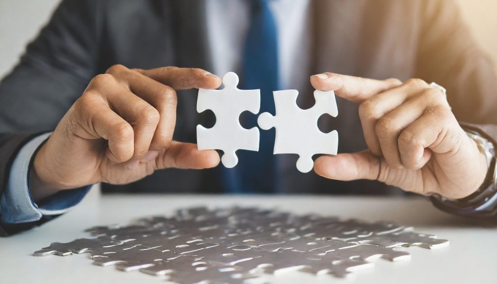 hands hold jigsaw puzzle on white table under bright backlight against clean blank wall
