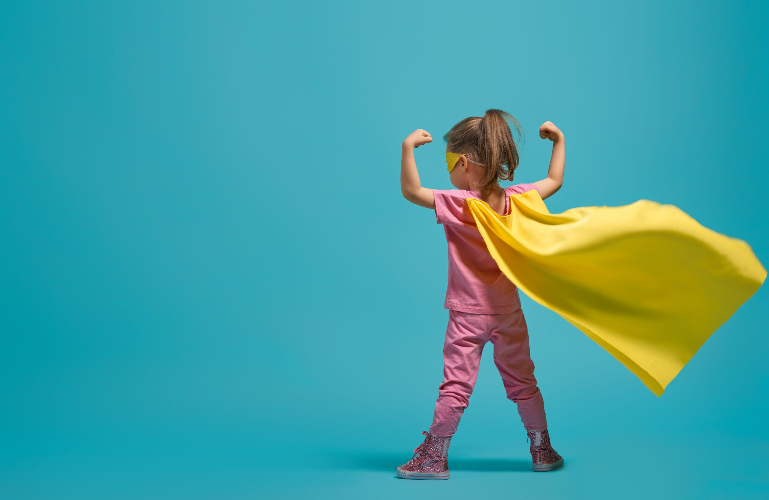 Little child playing superhero. Kid on the background of bright blue wall. Girl power concept. Yellow, pink and turquoise colors.